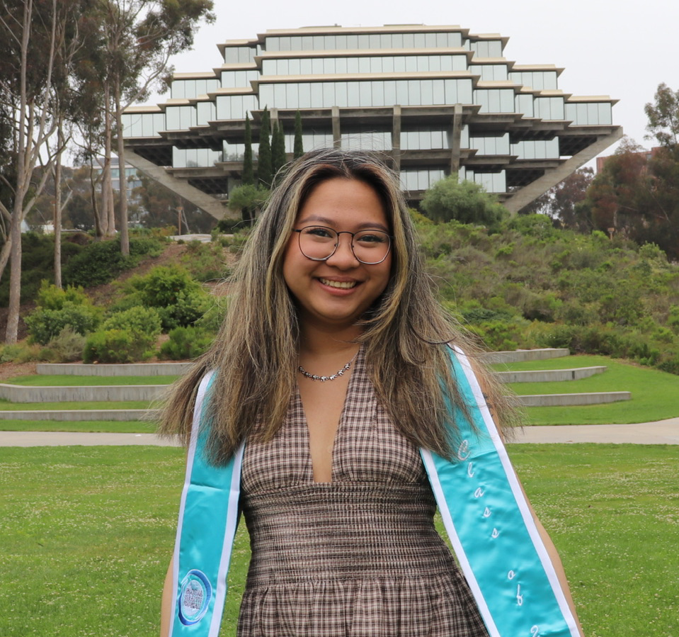Woman in cap and gown in front of building with grass in background smiling